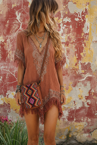 Woman wearing a bohemian-style dress with fringe and a patterned bag against a textured wall.