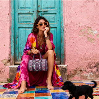 Woman in colorful outfit sitting on a colorful floor with a dog in front of a pink wall and blue door.