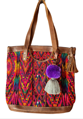 Colorful handbag with patterns and pom-poms hanging on a wooden door