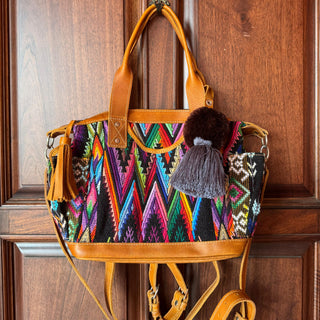 Colorful handbag with patterned design and tassels hanging on a wooden door.
