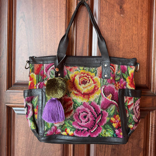 Colorful floral-patterned handbag with black handles hanging on a wooden door.