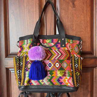 Colorful embroidered handbag with pom-poms hanging on a wooden door