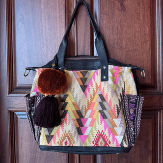 Colorful patterned handbag with pom-poms hanging on a wooden door.