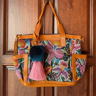Colorful embroidered handbag with floral patterns and tassels hanging on a wooden door.