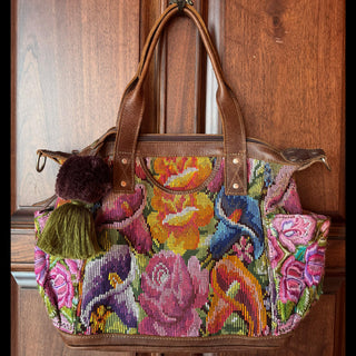Colorful embroidered handbag with floral and bird patterns hanging on a wooden door.