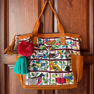 Colorful patterned handbag with brown handles hanging on a wooden door.