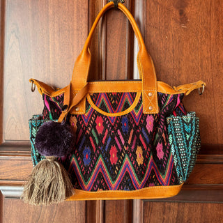 Colorful handbag with patterned design and leather handle against a wooden door background