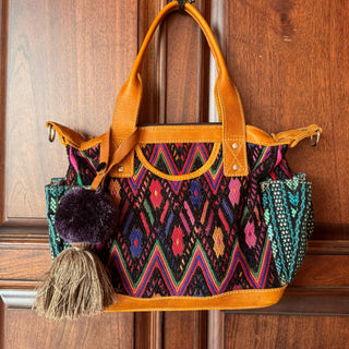 Colorful handbag with patterned design and brown handle against a wooden background