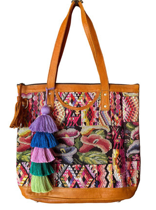 Colorful patterned handbag with leather handle hanging on a wooden door.