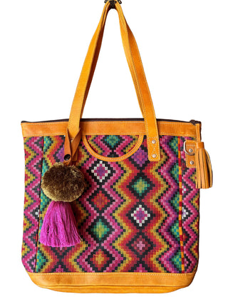 Colorful handbag with geometric pattern and tassels hanging on a wooden door.