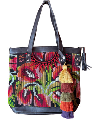 Colorful handbag with floral patterns and tassels hanging on a wooden door.