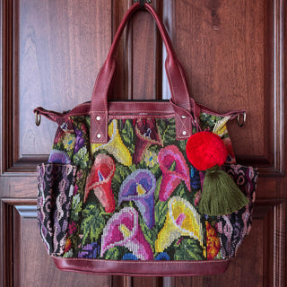 Colorful embroidered handbag with floral patterns and a red pom-pom on a wooden door.