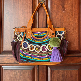 Colorful handbag with decorative patterns and tassels hanging on a wooden door.