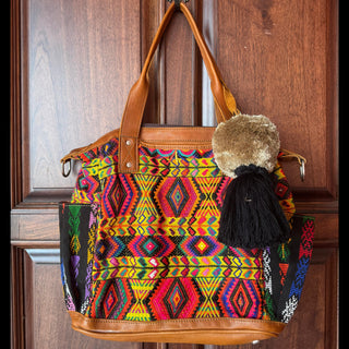 Colorful patterned handbag with brown leather handle and trim hanging on a wooden door.