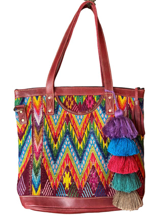 Colorful handbag with geometric pattern and tassels hanging on a wooden door.