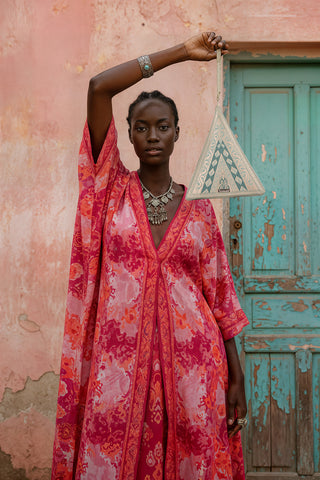 Woman in a vibrant red dress holding a geometric-patterned bag against a textured wall and blue door.