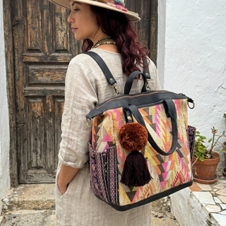 Woman with a colorful backpack and decorative hat standing in front of a wooden door.