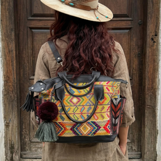 Person wearing a colorful backpack with a pattern, standing in front of a wooden door.