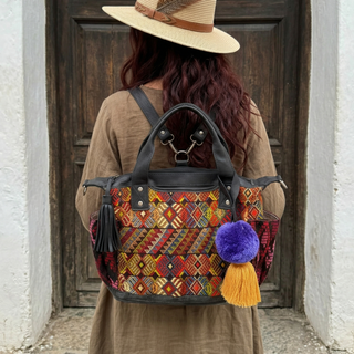 Person wearing a colorful backpack with geometric patterns and tassels, standing in front of a wooden door.
