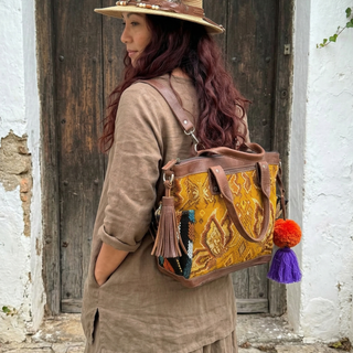Woman wearing a straw hat with a feather and carrying a decorative bag in front of a wooden door.