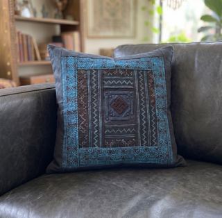 Decorative pillow with blue and brown patterns on a gray sofa in a living room setting.